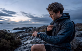 Trailrunner prüft bei nassem Wetter an einer Felsküste seine runde Outdoor-Sportuhr