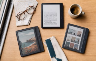 Drei E-Reader mit Schwarz-Weiß-Text, Farbillustration und Bibliotheksansicht auf einem Holztisch im Zug