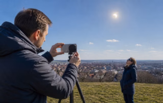 Zwei Menschen fotografieren eine partielle Sonnenfinsternis sicher mit gefiltertem Smartphone und Finsternisbrille