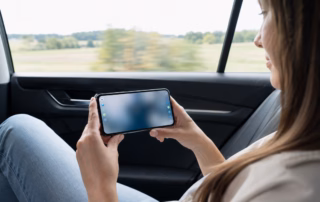 Beifahrerin hält ein neutrales Smartphone mit kleinen farbigen Punkten an den Bildschirmrändern